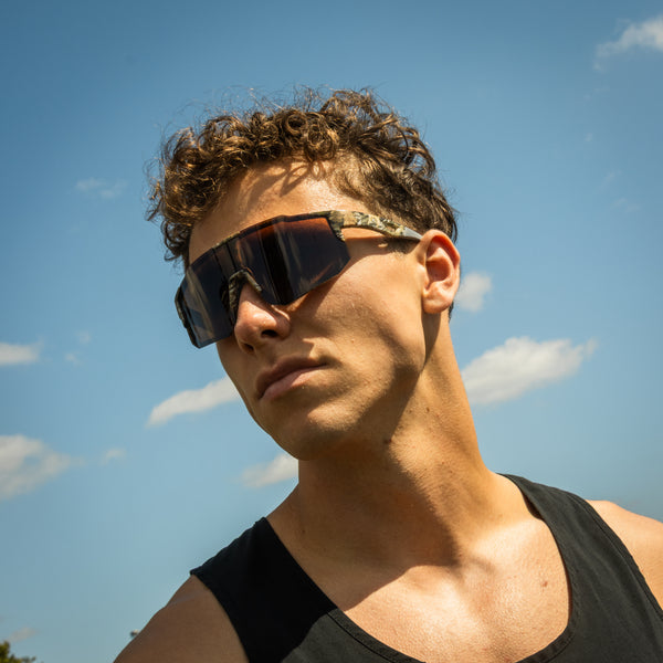 Mand bærer Noire Camo sportsbriller med army mønster mod blå himmel