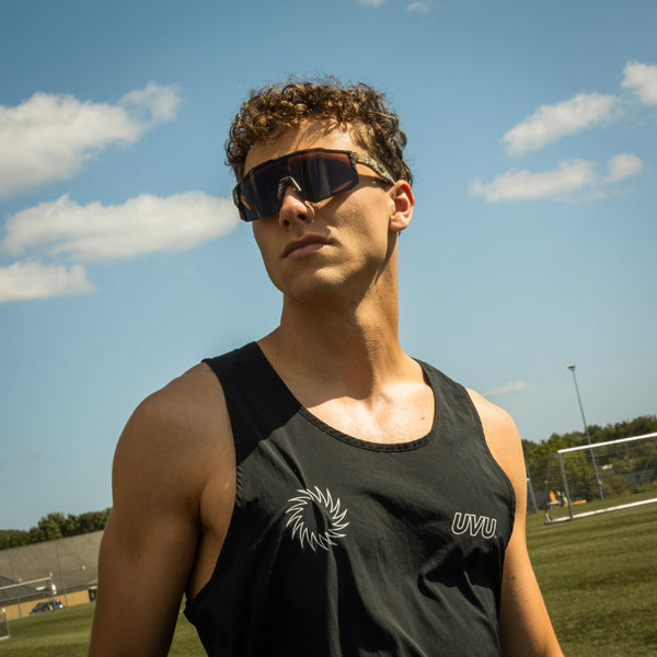 Mand bærer Noire Camo sportsbriller i army-farve udendørs under blå himmel