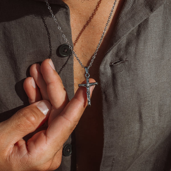 Sølvfarvet kors halskæde med Jesus-figur holdt i hånden