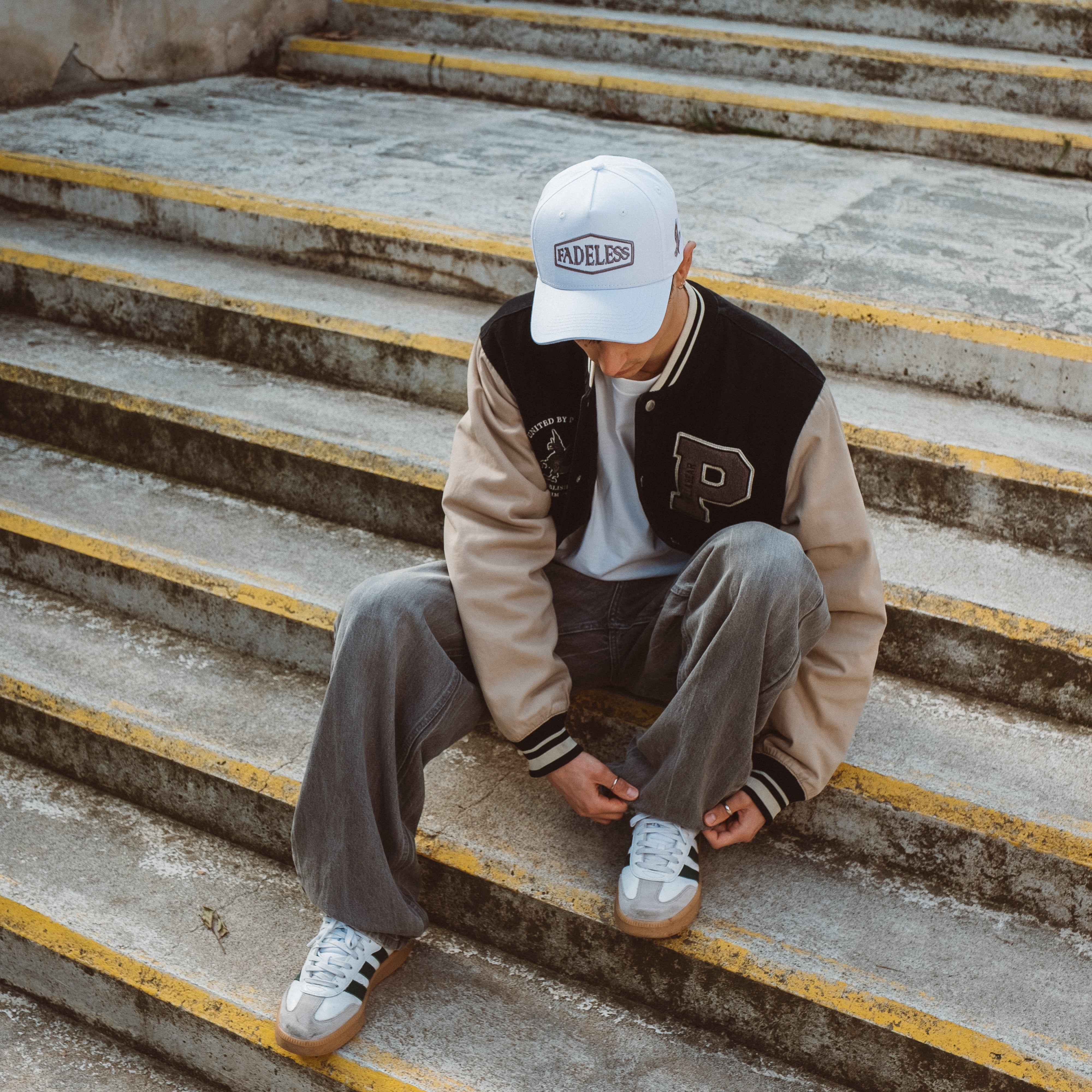 Hvid Fadeless kasket med college jakke og sneakers på trappe