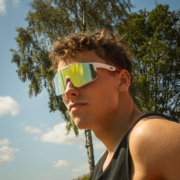 Sportsbriller med gult spejlglas og hvid stel båret udendørs af atlet