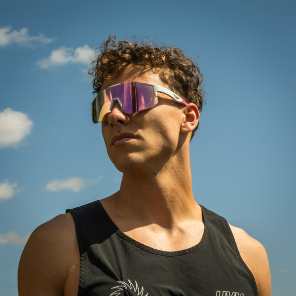 Mand bærer Noire Glamour sportsbriller i lyserød med spejlglas under blå himmel