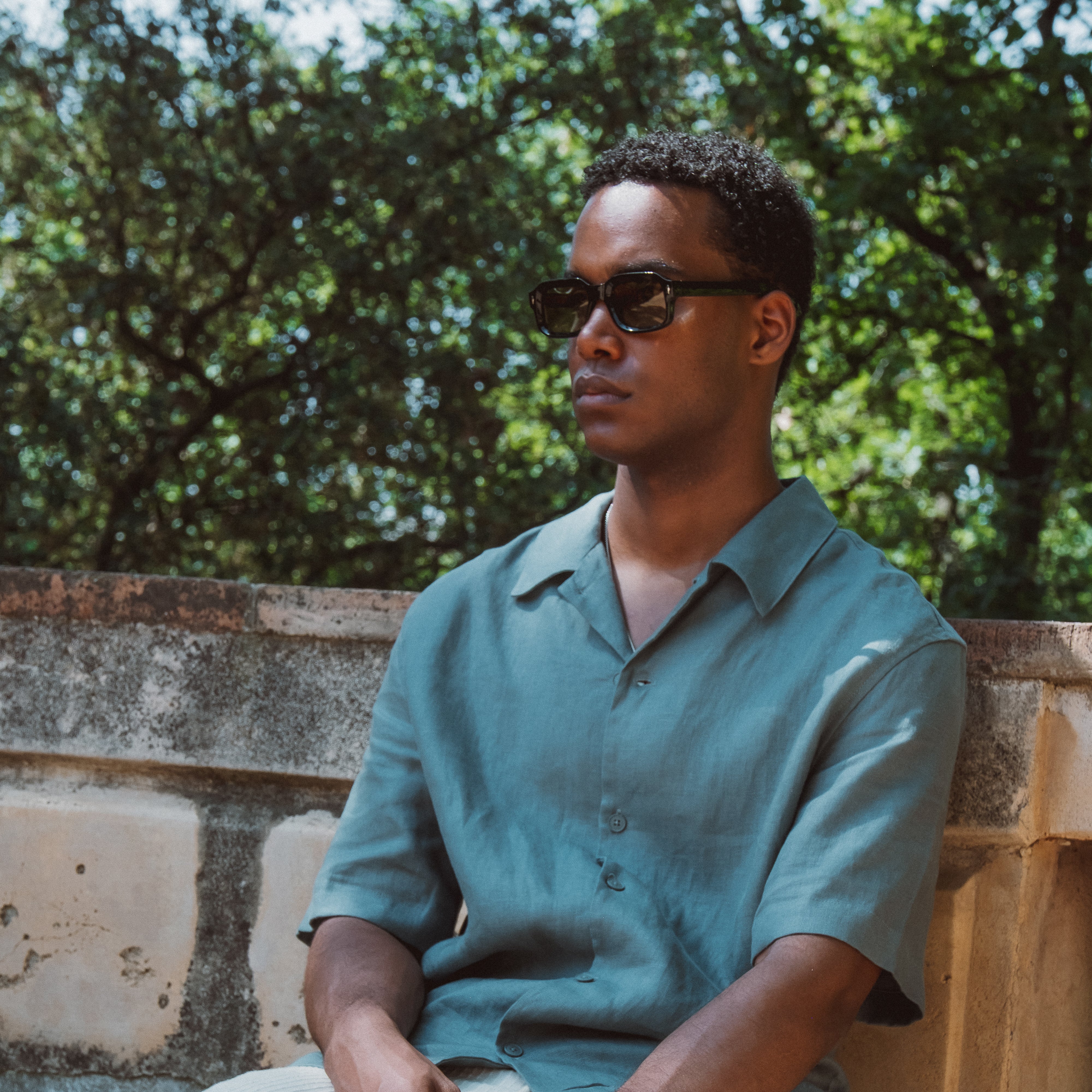 Mand iført Hugo Blackout solbriller i sort med grøn skjorte udendørs