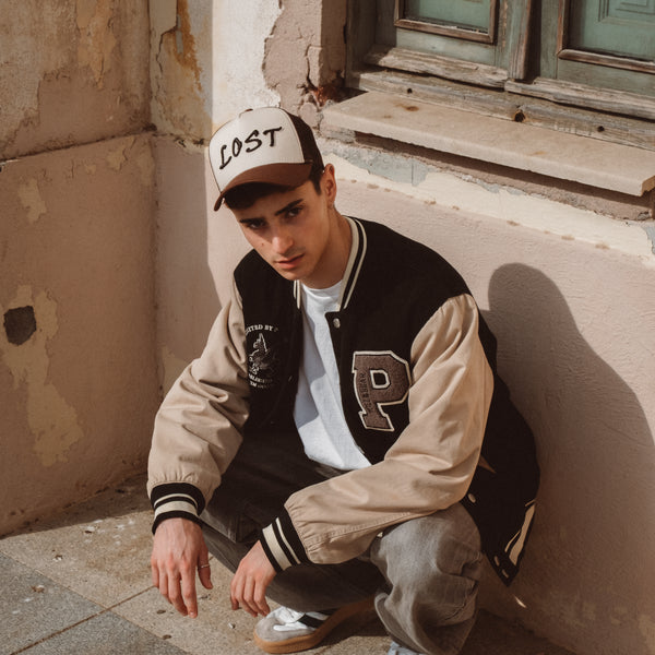 Ung mand i college-jakke og LOST kasket sidder ved gammel mur