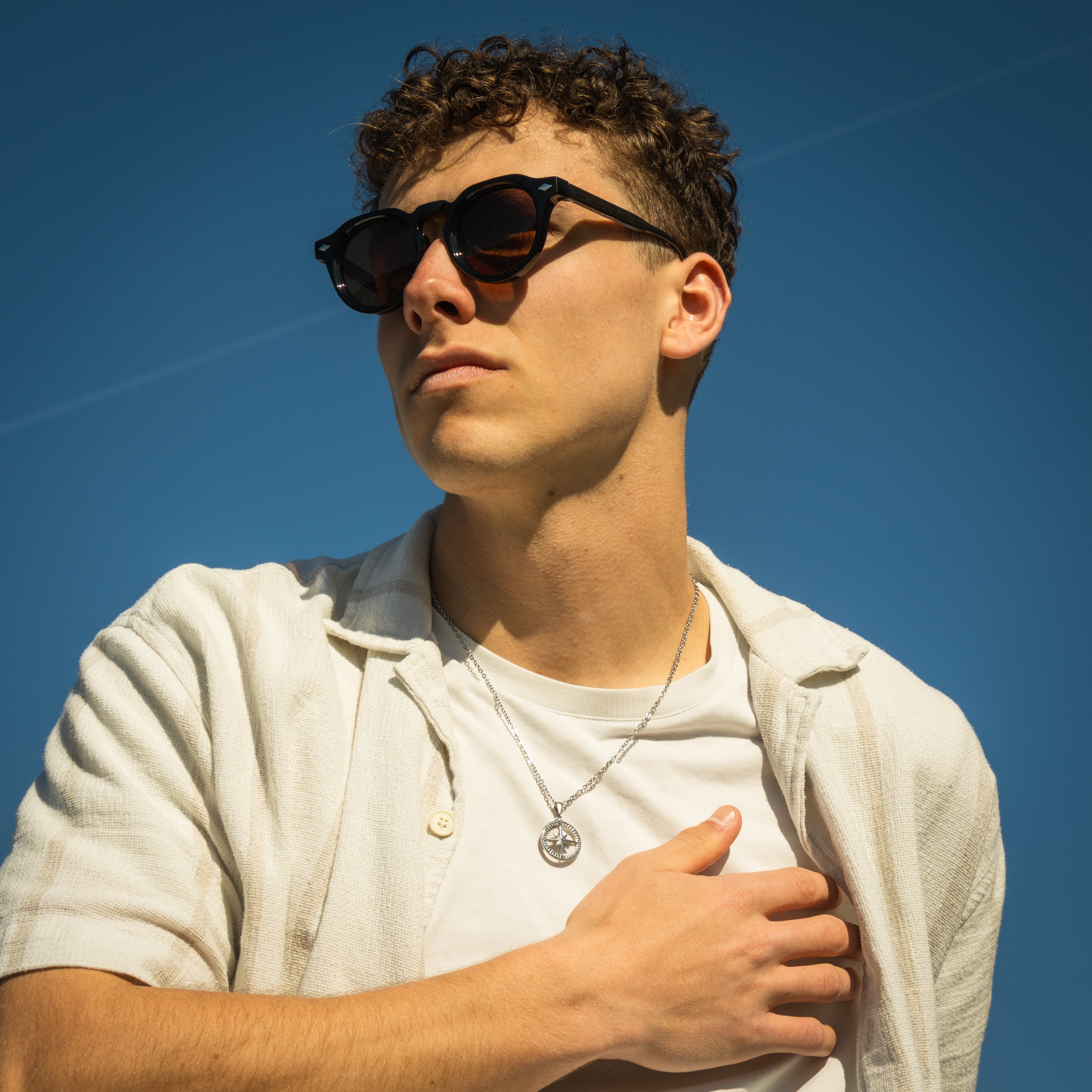 Loui Dusky solbriller i brun på model med krøllet hår mod blå himmel