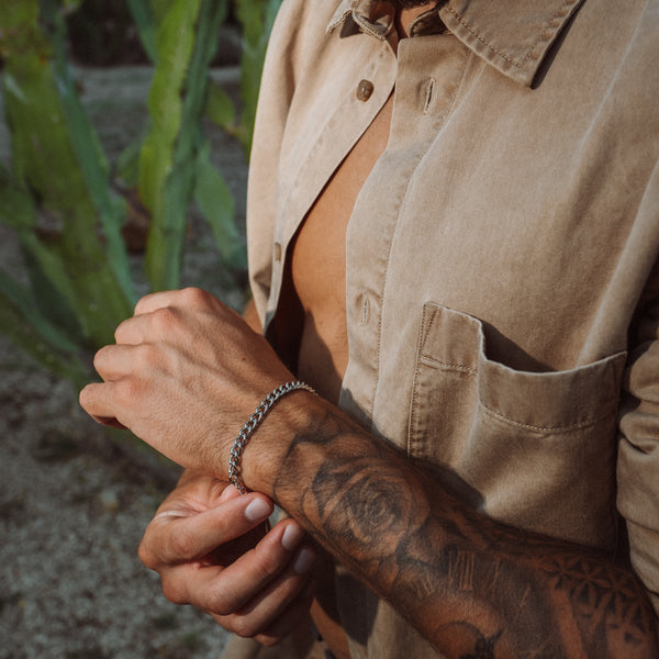 Mand bærer sølvfarvet kæde armbånd med beige skjorte og tatovering