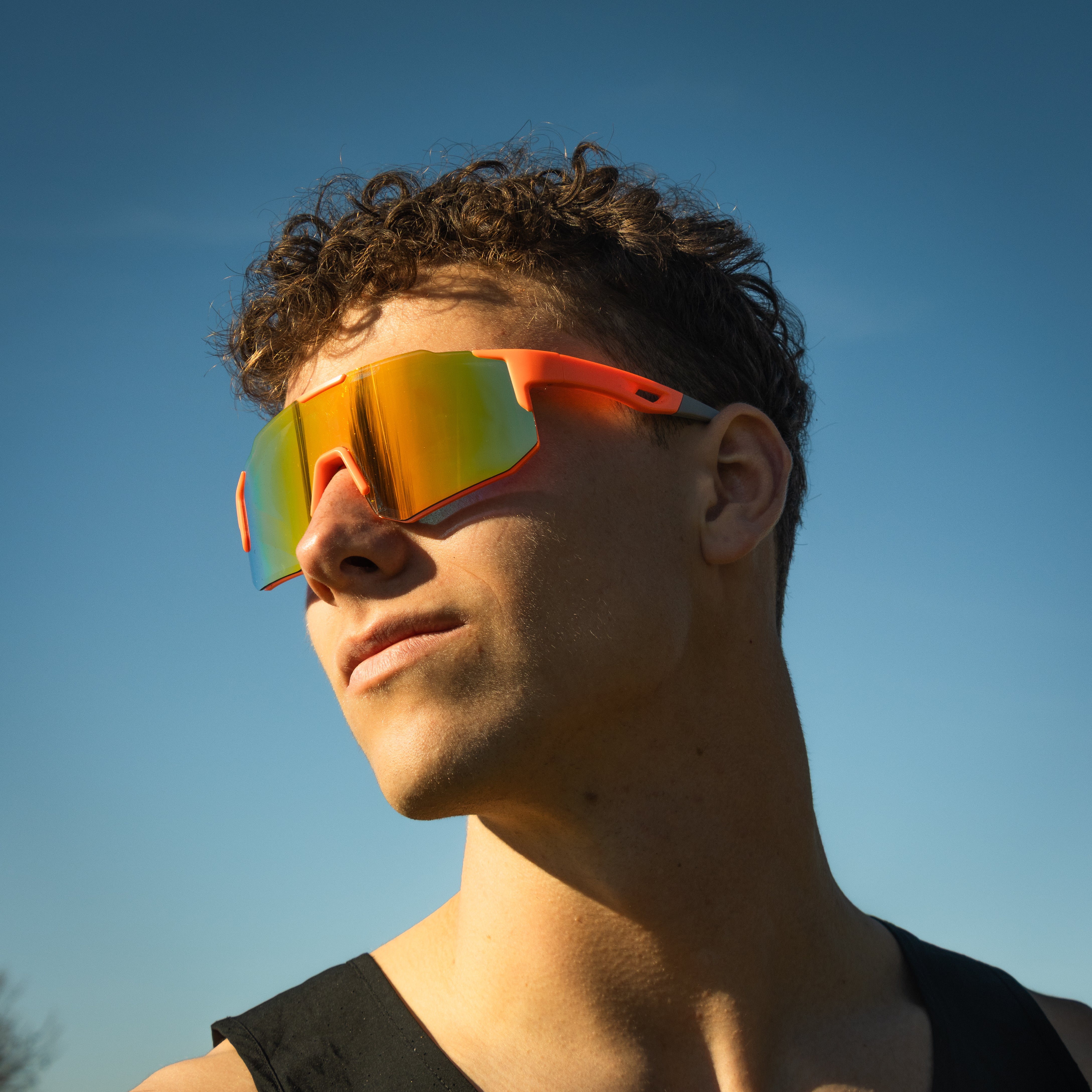 Sportsbriller i orange med spejlglas på model mod blå himmel