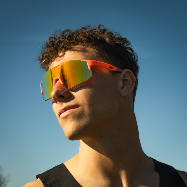 Sportsbriller i orange med spejlglas på model mod blå himmel