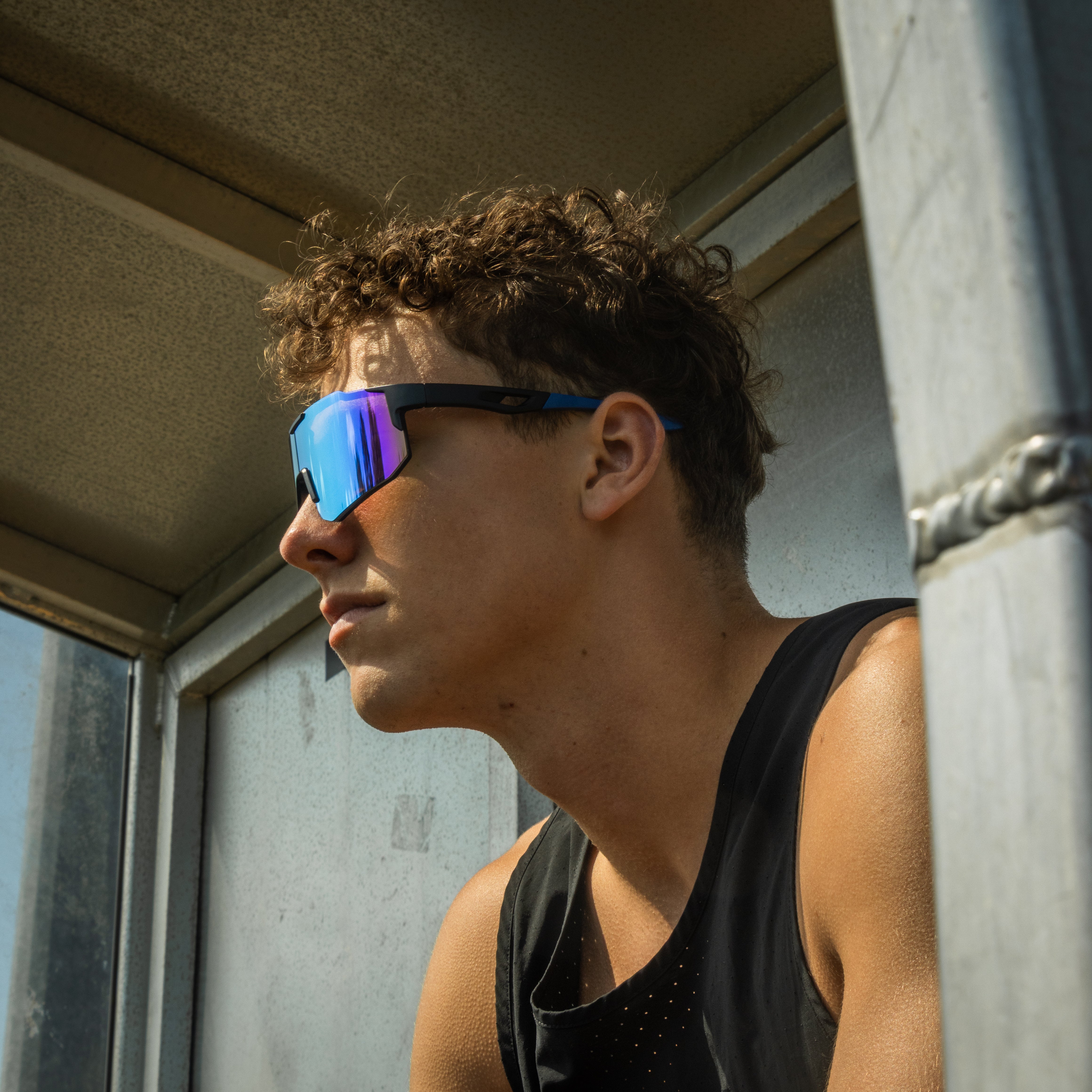 Sportsbriller med blå spejlglas og sort stel på model i profil