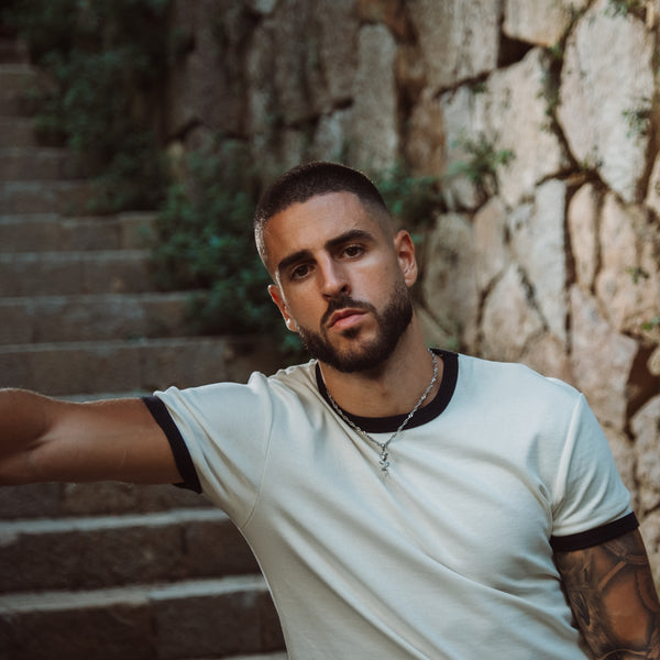 Mand iført hvid t-shirt med sølvfarvet halskæde med kors-vedhæng