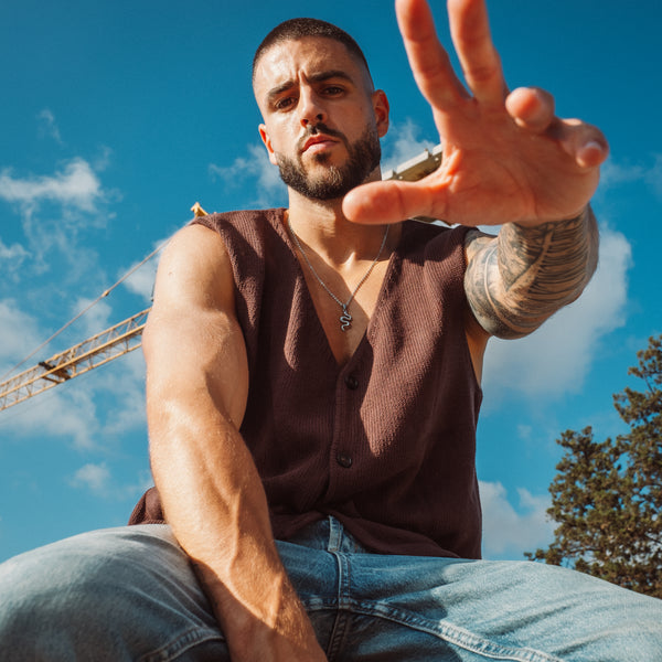 Mand bærer sølvfarvet snake halskæde med tatoveringer og brun vest