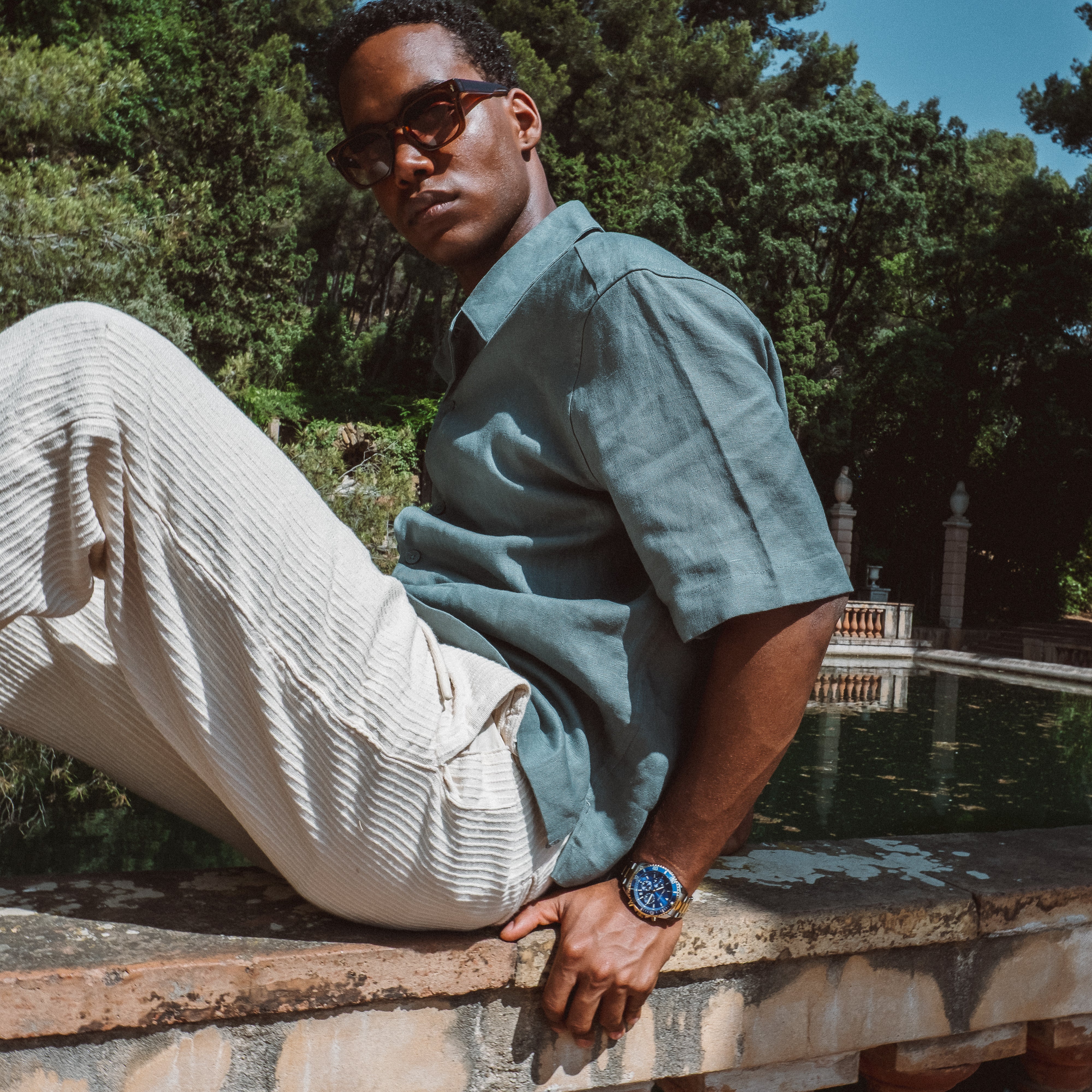 Mand iført grøn kortærmet skjorte og beige shorts med solbriller udendørs