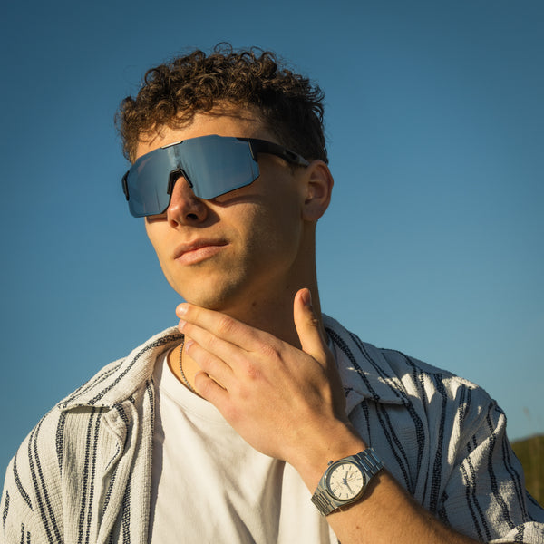Mand med Noire Steely sportsbriller i grå med blå spejlglas mod blå himmel