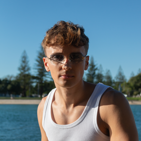 Mand med solbriller og hvid tanktop ved stranden under blå himmel