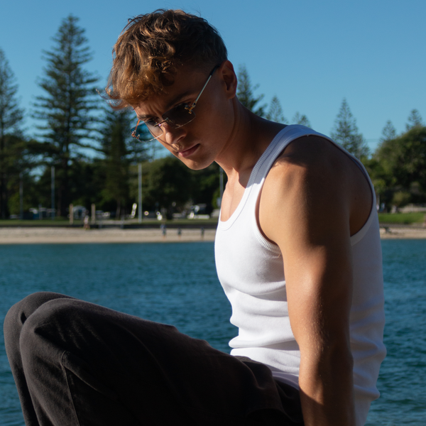 Ung person i hvid tanktop med solbriller ved stranden