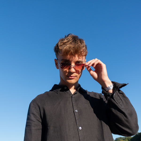 Ung mand med brune solbriller og sort skjorte mod blå himmel