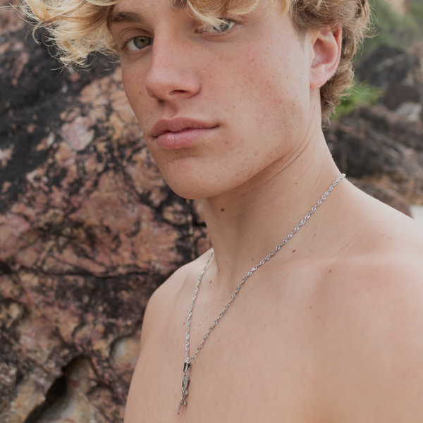 Ung mand bærer sølvfarvet halskæde med rose-vedhæng
