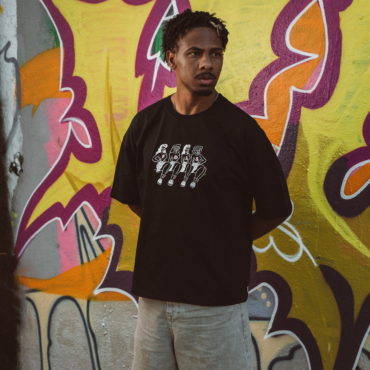 Mand i sort oversized Chicks Tee foran farverig graffiti væg