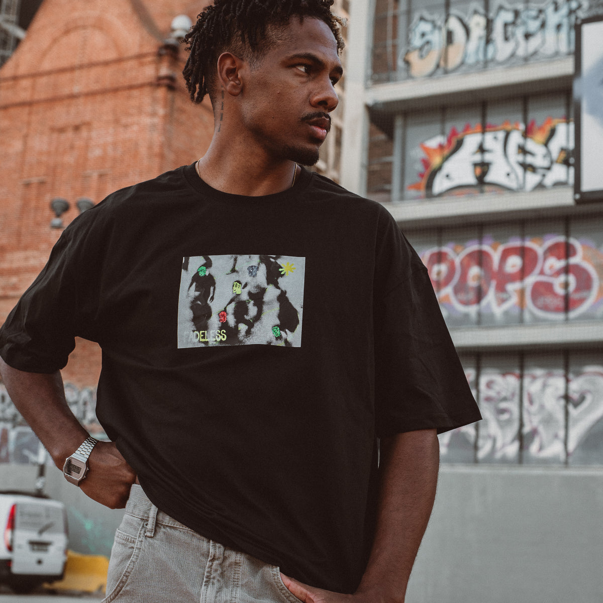 Mand i sort oversized t-shirt med grafisk print foran graffiti-væg