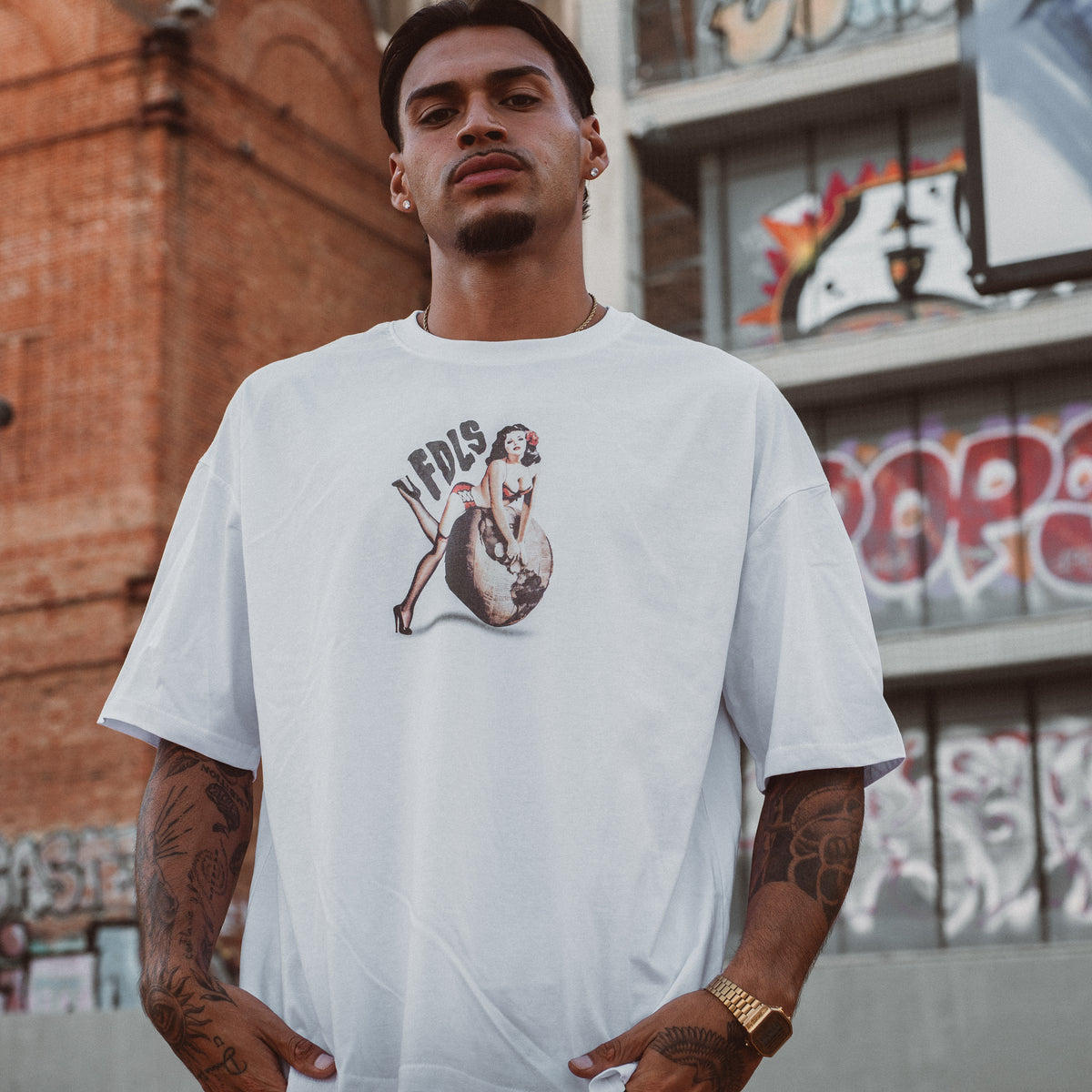 Mand i hvid oversized t-shirt med vintage grafik foran mursten og graffiti