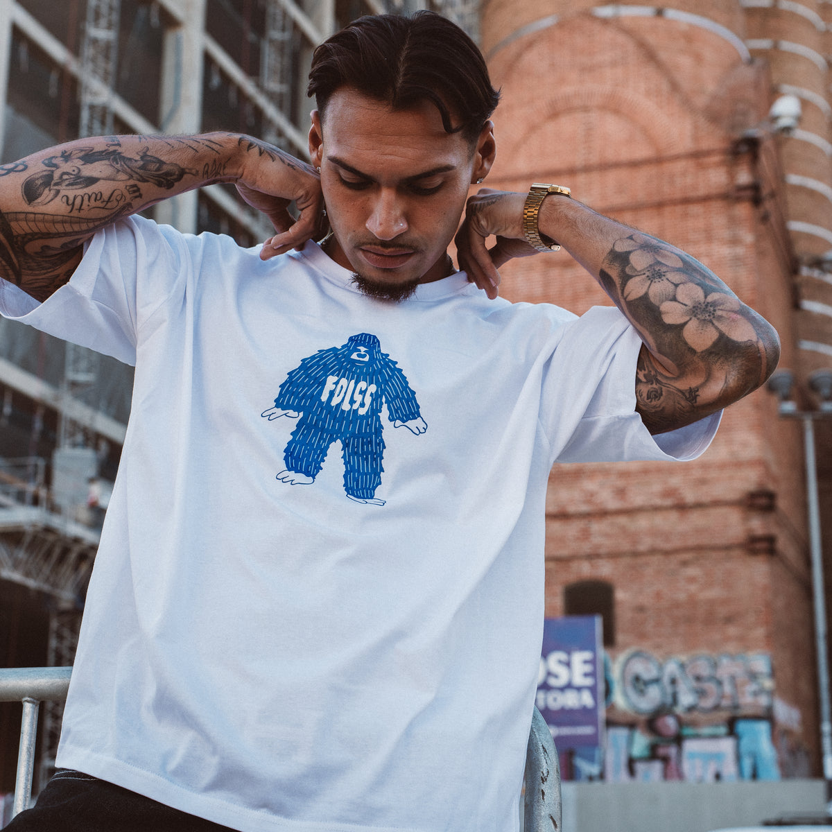 Mand med tatoveringer iført hvid oversized Ray Tee med blåt monster-print fra Fadeless